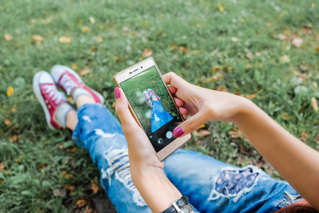 A girl aims her smartphone camera at her shoes while she is laying down on the grass