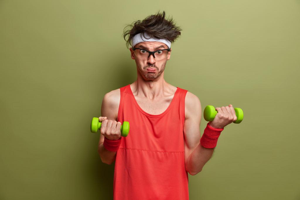 thin man in glasses wearing headband while lifting small green weights