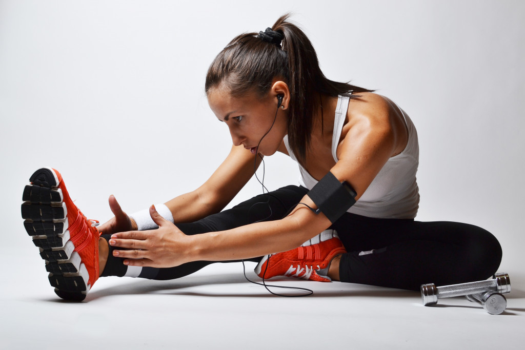 female athlete in ponytail with headset and red shoes stretching