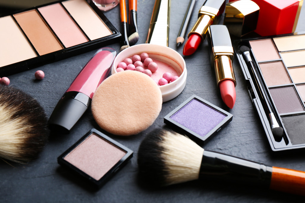 Makeup kit consisting of a blush-on, brush, and lipstick on a table.