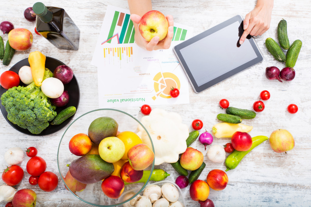 person holding an apple while reviewing charts and research on tablet about veganism