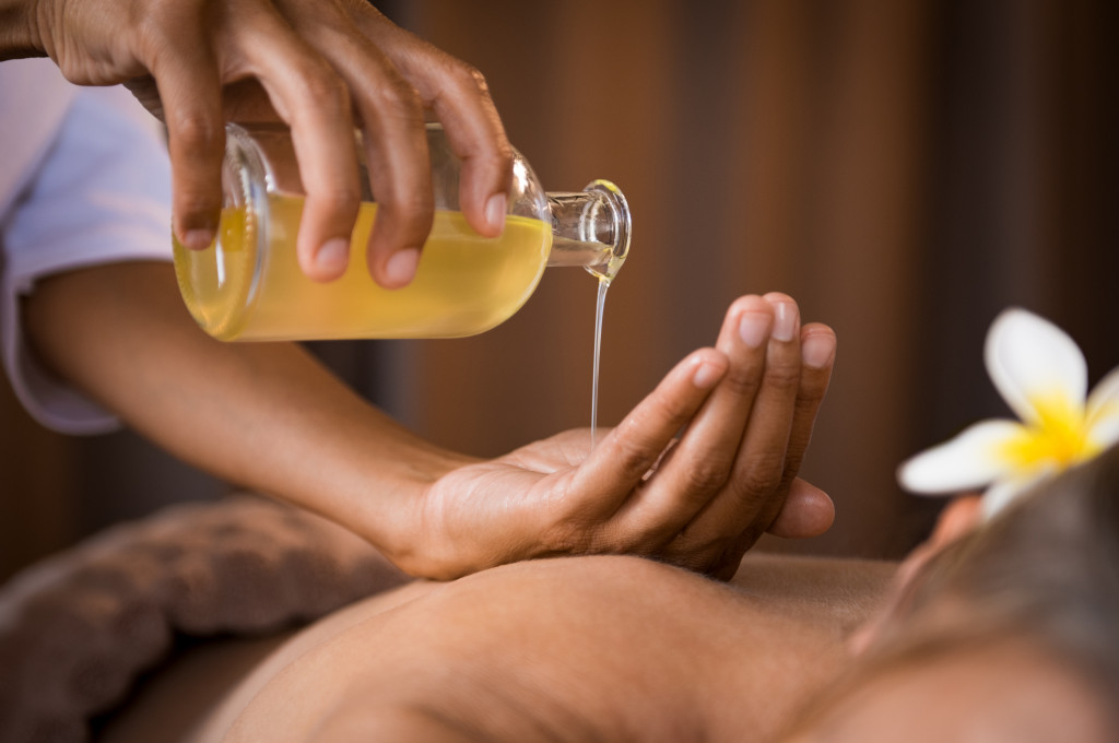 woman pouring massage oils in her hands to massage a lying down man in a spa